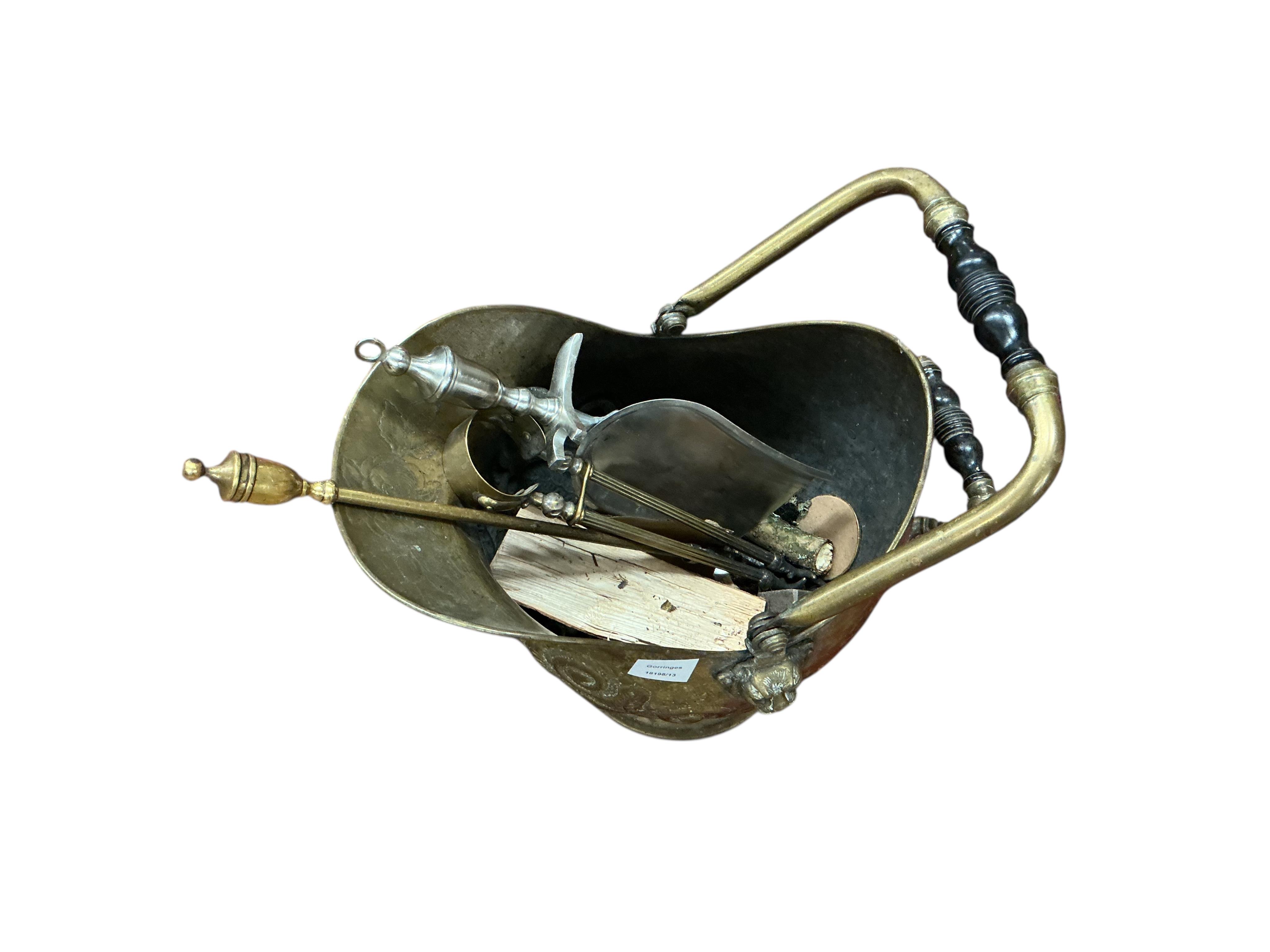 An embossed brass helmet shaped coal scuttle and assorted fire implements